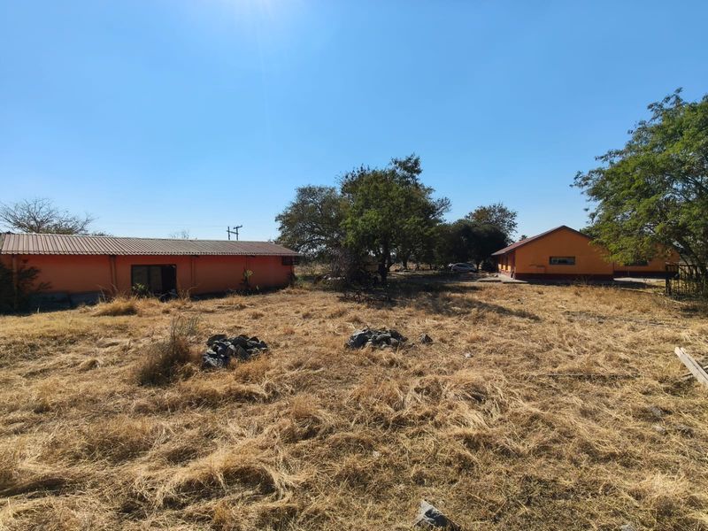 View of the rear farm property grounds featuring multiple outbuildings with metal roofing and orange exterior walls set within a dry landscape.