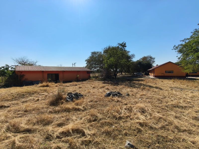 A view of the rear farm grounds featuring two detached outbuildings with orange plastered walls and corrugated metal roofing under a clear sky.