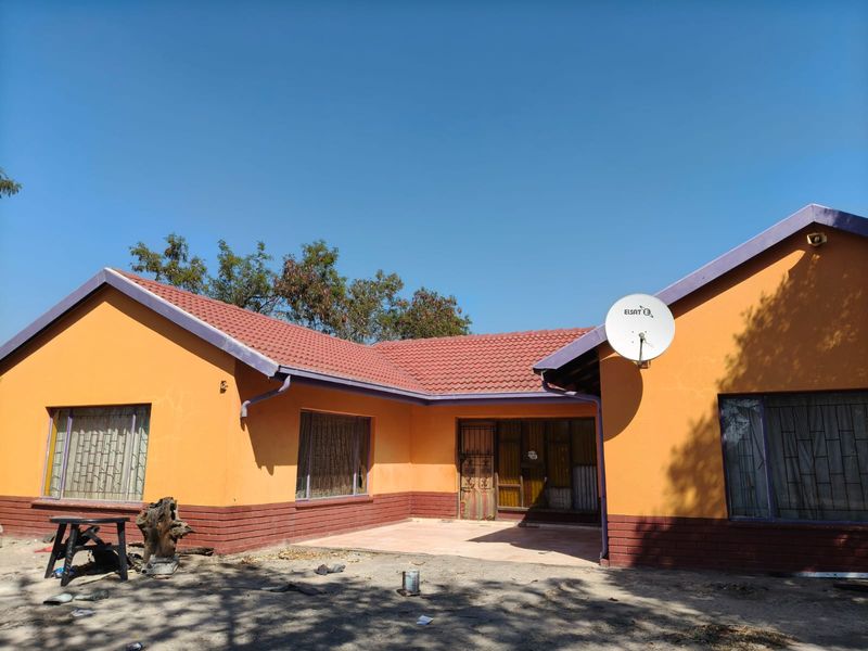Rear view of a farm-style house featuring a tiled roof, brick plinth, and a paved patio area with security gate access.
