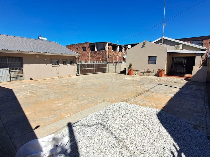 A spacious paved rear courtyard area featuring perimeter security fencing and access to the main building structures.
