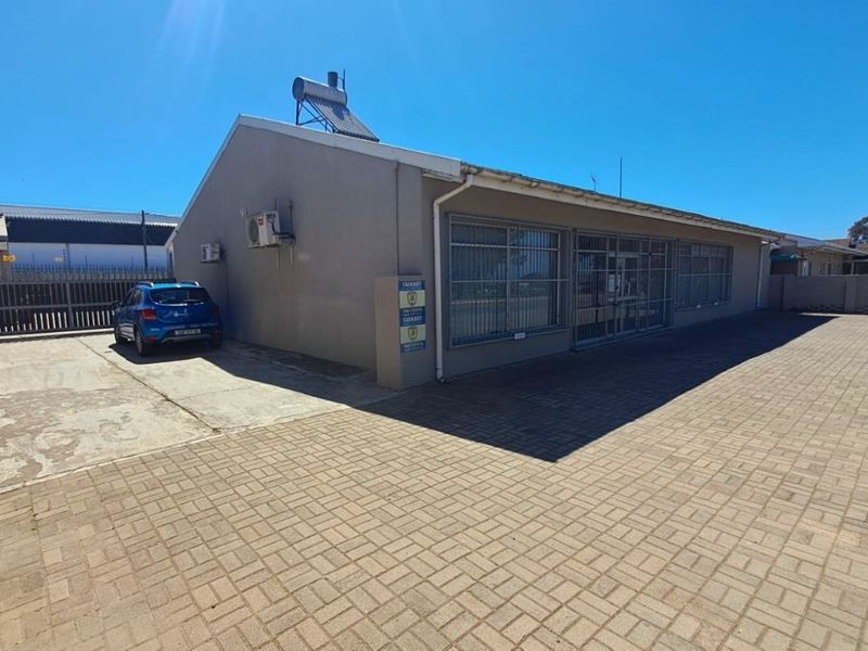Exterior view of a commercial property featuring paved parking area, security bars on windows, and a solar water heating system on the roof.