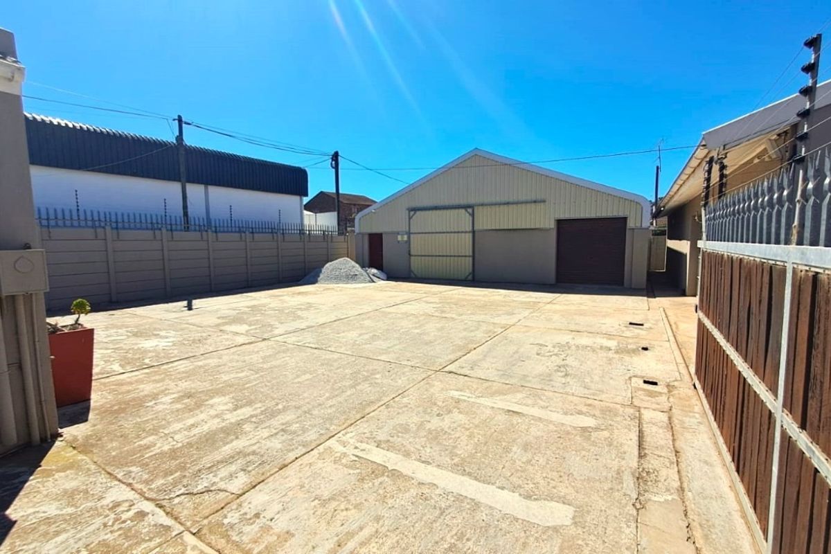 Spacious paved rear yard area featuring a large industrial-style storage building with sliding doors and secure perimeter walling with electric fencing.