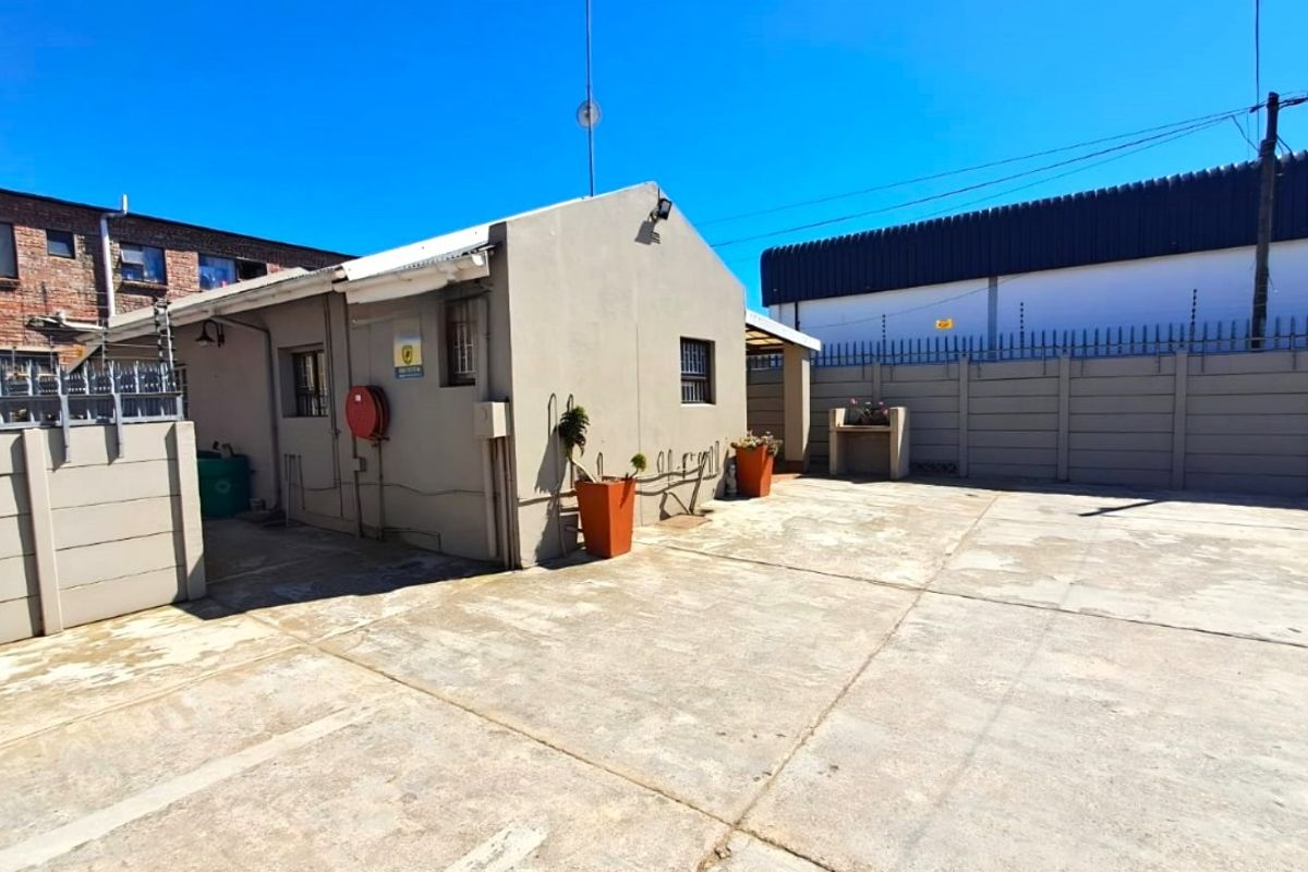 Exterior rear view of the business property featuring a paved courtyard, perimeter wall with security fencing, and a built-in outdoor braai area.