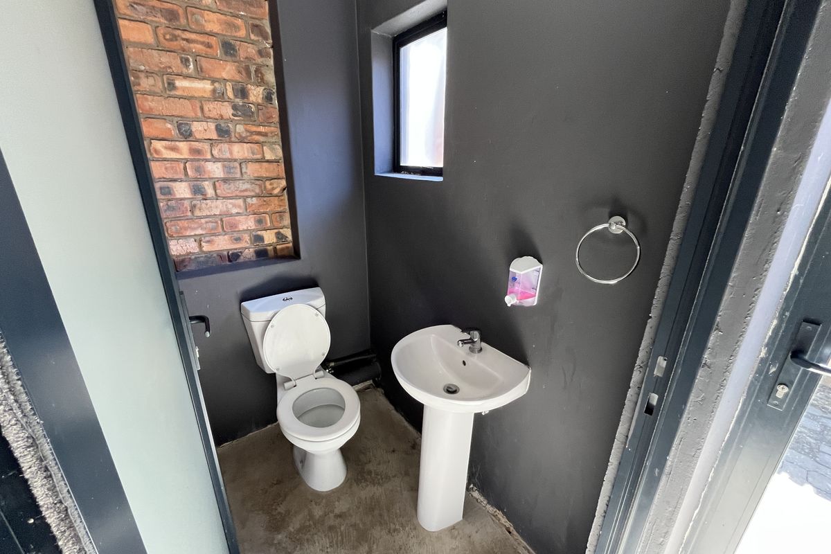 Compact restroom featuring a pedestal basin, toilet, and modern dark-painted walls with an exposed brick accent feature.