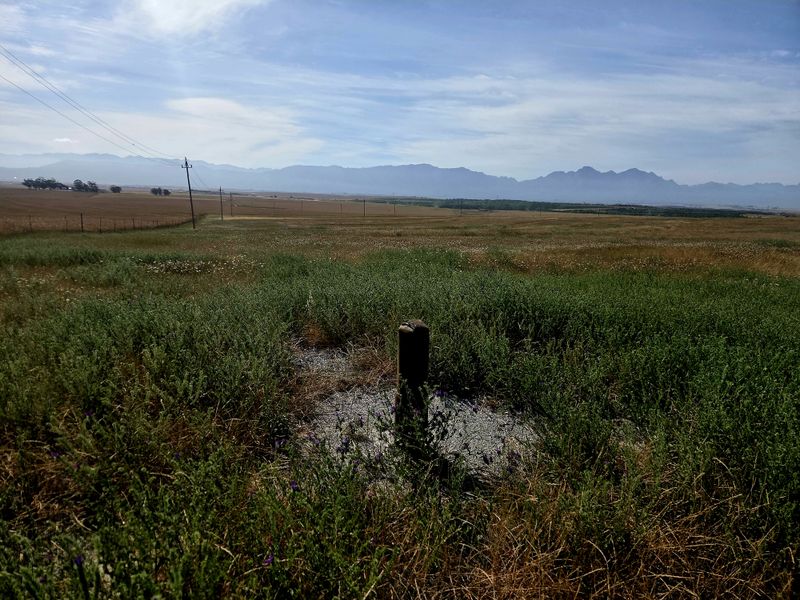 Expansive rural landscape view featuring open fields, distant mountain ranges, and existing utility infrastructure.