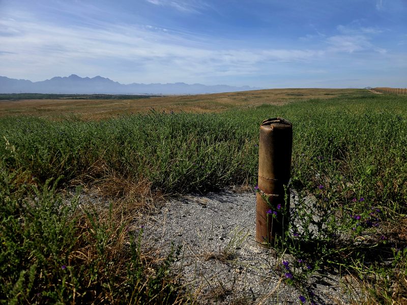 Expansive rural landscape view featuring a metal borehole casing set within open farmland under a clear blue sky.