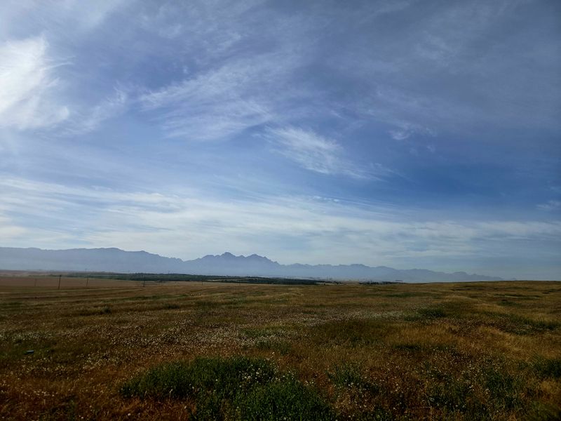 Expansive landscape view featuring open fields and distant mountain ranges under a clear blue sky.