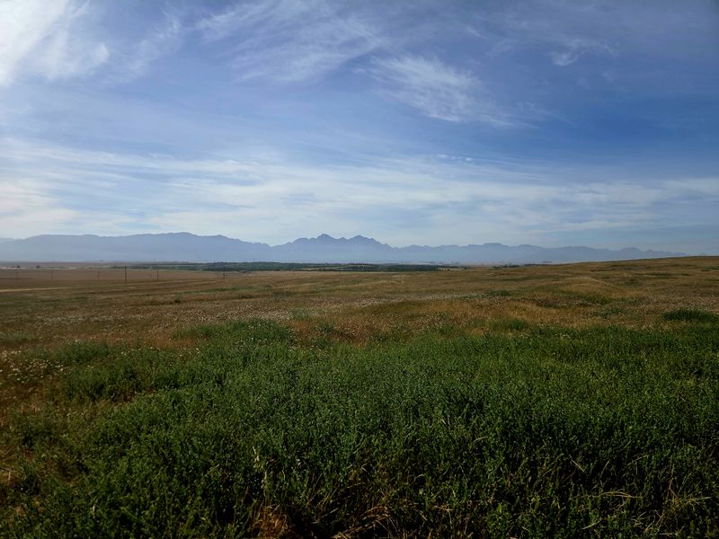 Expansive panoramic view of the open farm landscape featuring rolling fields and distant mountain ranges under a clear blue sky.