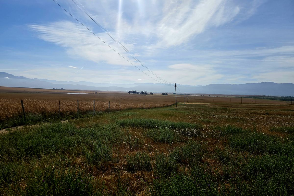 Expansive view of open farmland and fields with distant mountain ranges under a clear blue sky.