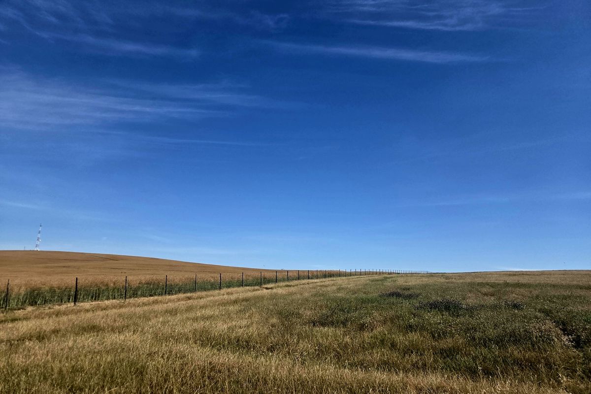 Expansive view of open farmland featuring rolling fields and perimeter wire fencing under a clear blue sky.