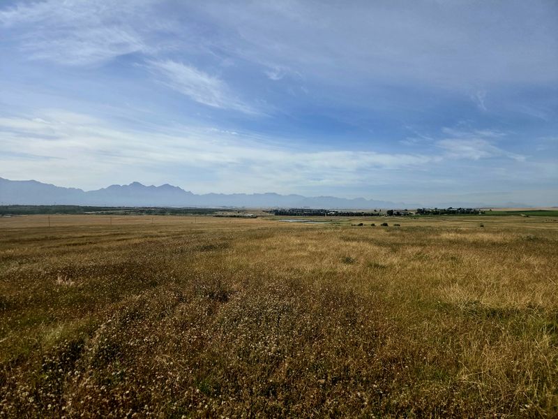 A scenic, expansive view of the open farm landscape featuring rolling fields and a distant mountain range under a clear blue sky.
