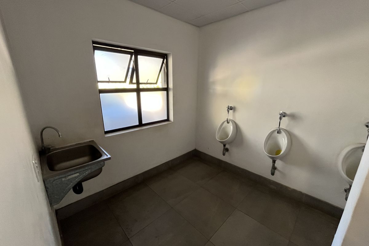 Functional industrial restroom facility featuring three wall-mounted urinals, a stainless steel basin, and tiled flooring.