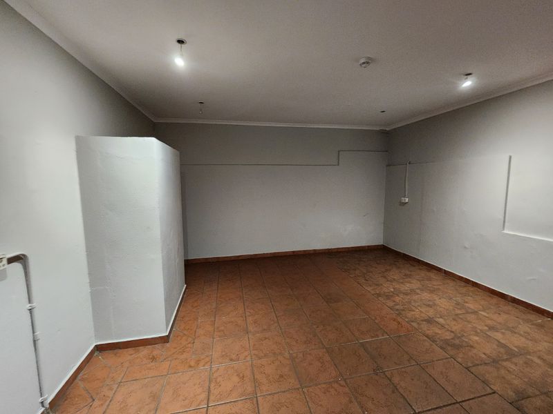 An empty, functional utility space featuring tiled flooring, recessed lighting, and exposed electrical conduit, suitable for various industrial or storage applications.