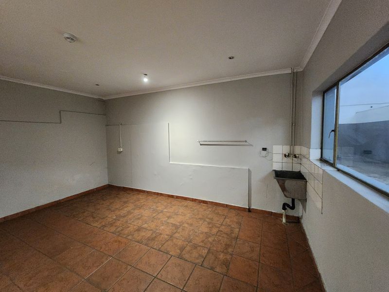A functional, empty utility or laundry space featuring tiled flooring, a wall-mounted sink, and exposed plumbing connections.