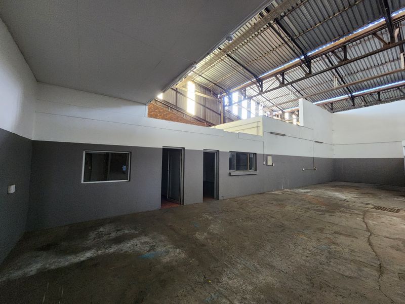 Spacious industrial utility area featuring high exposed steel roof trusses, concrete flooring, and internal office partitions, suitable for workshop or storage use.
