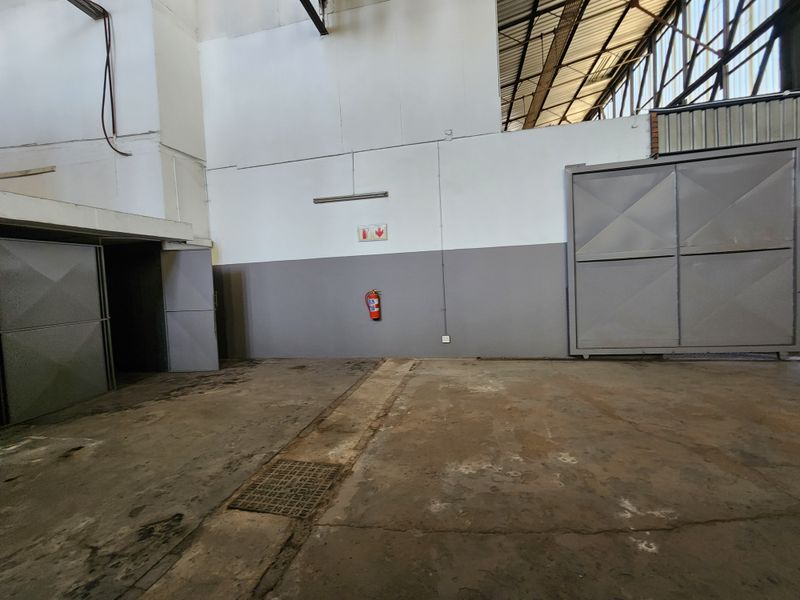Spacious industrial utility area featuring concrete flooring, metal sliding doors, and exposed roof trusses, suitable for storage or workshop operations.