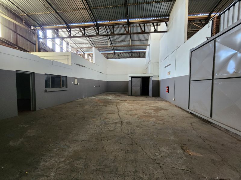 Spacious industrial utility area featuring high exposed steel roof trusses, concrete flooring, and functional metal access doors.