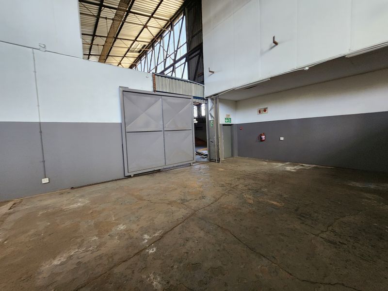 Spacious industrial utility area featuring high-bay ceilings, exposed steel roof structure, large sliding access door, and durable concrete flooring.