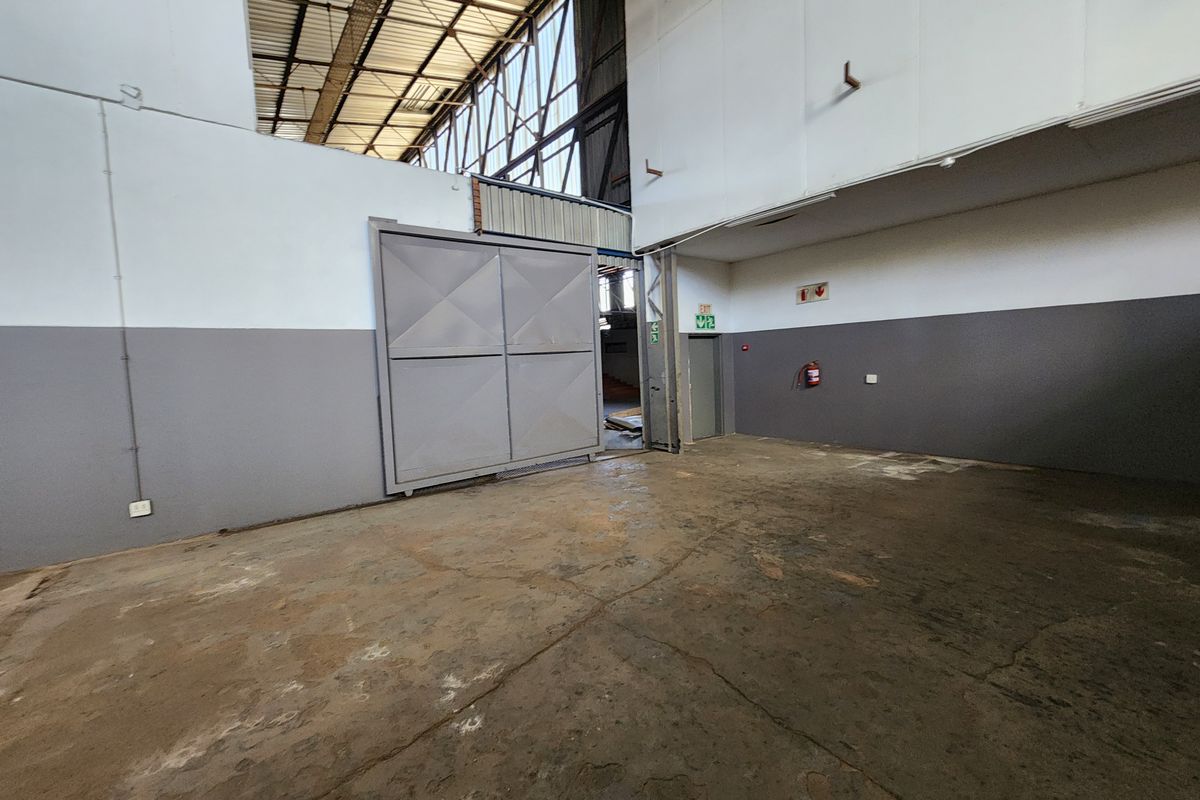Spacious industrial utility area featuring high-bay ceilings, exposed steel roof structure, large sliding access door, and durable concrete flooring.