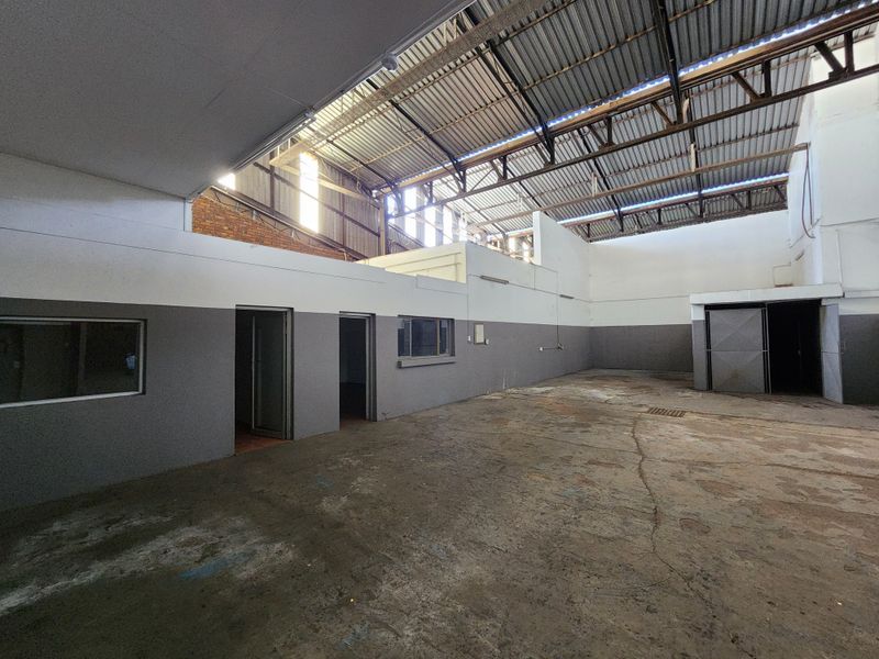 Spacious industrial utility area featuring high exposed steel roof trusses, concrete flooring, and integrated office partitions, suitable for workshop or storage use.
