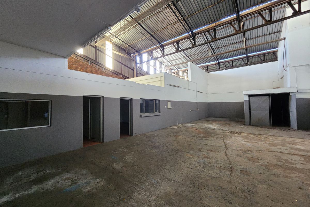 Spacious industrial utility area featuring high exposed steel roof trusses, concrete flooring, and integrated office partitions, suitable for workshop or storage use.