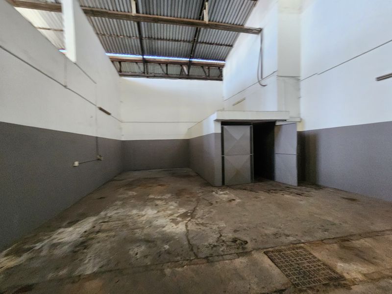 An empty industrial utility space featuring high ceilings with exposed corrugated metal roofing, concrete flooring with drainage, and painted wall finishes.