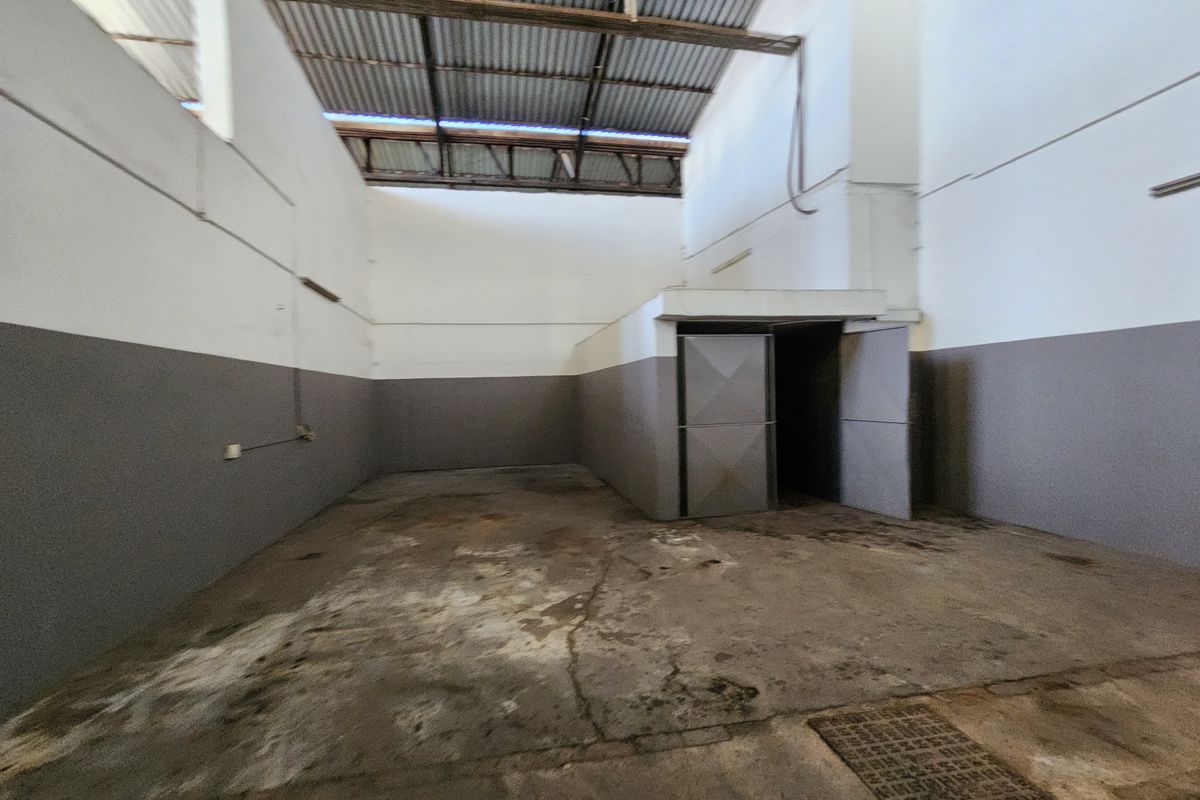 An empty industrial utility space featuring high ceilings with exposed corrugated metal roofing, concrete flooring with drainage, and painted wall finishes.