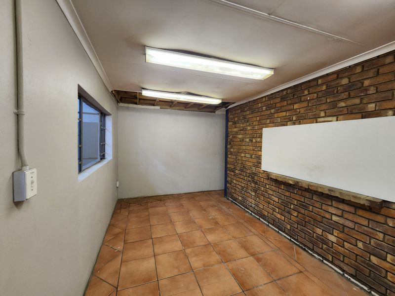 An empty office space featuring exposed brickwork, tiled flooring, and fluorescent lighting, currently requiring ceiling repairs and general maintenance.