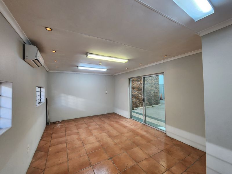 A clean, empty office space featuring tiled flooring, air conditioning, and a sliding glass door providing access to an exterior area.