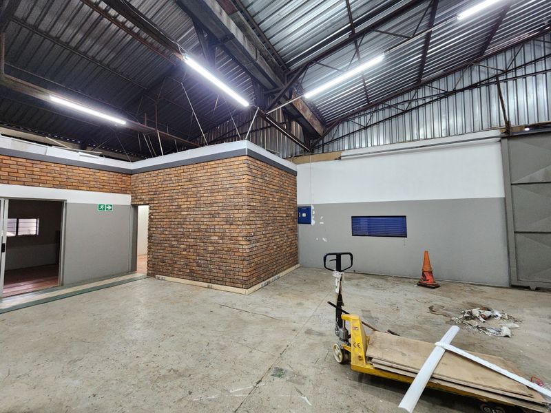 Spacious industrial utility area featuring high ceilings with exposed steel trusses, durable concrete flooring, and a central face brick partition wall.