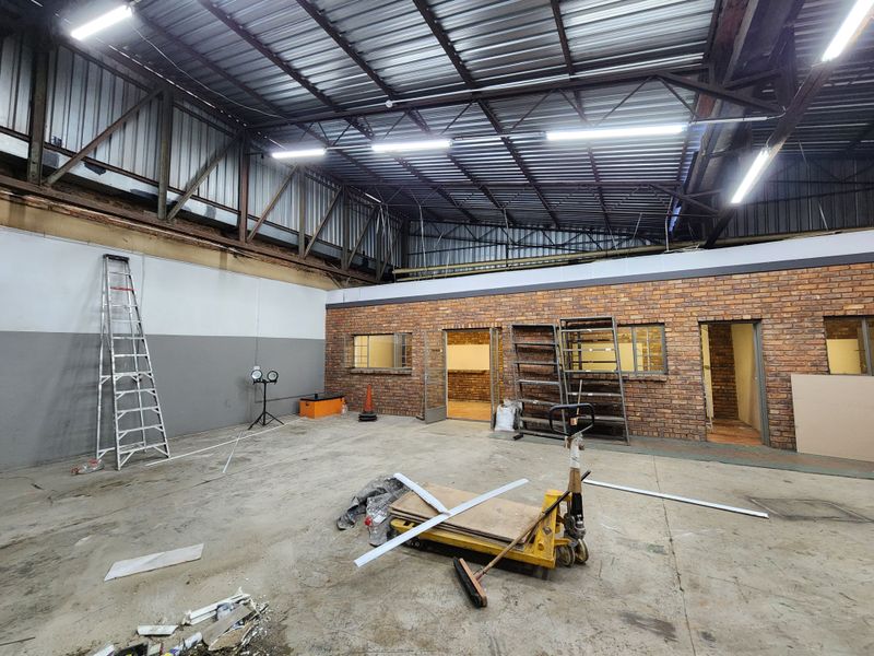 Spacious industrial utility area featuring exposed steel roof trusses, brick wall finishes, and concrete flooring, suitable for workshop or storage use.