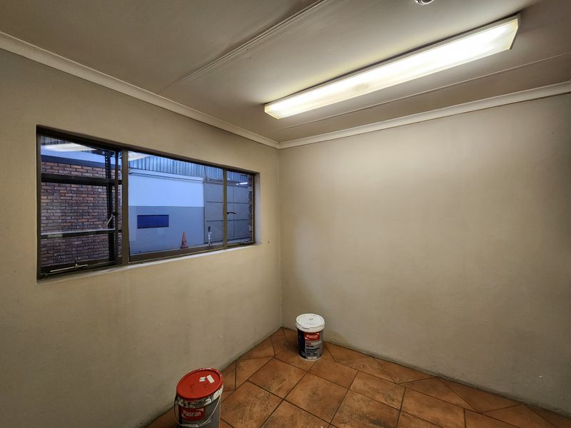 A vacant office space featuring tiled flooring, neutral walls, and a large window providing natural light, suitable for a professional workspace.