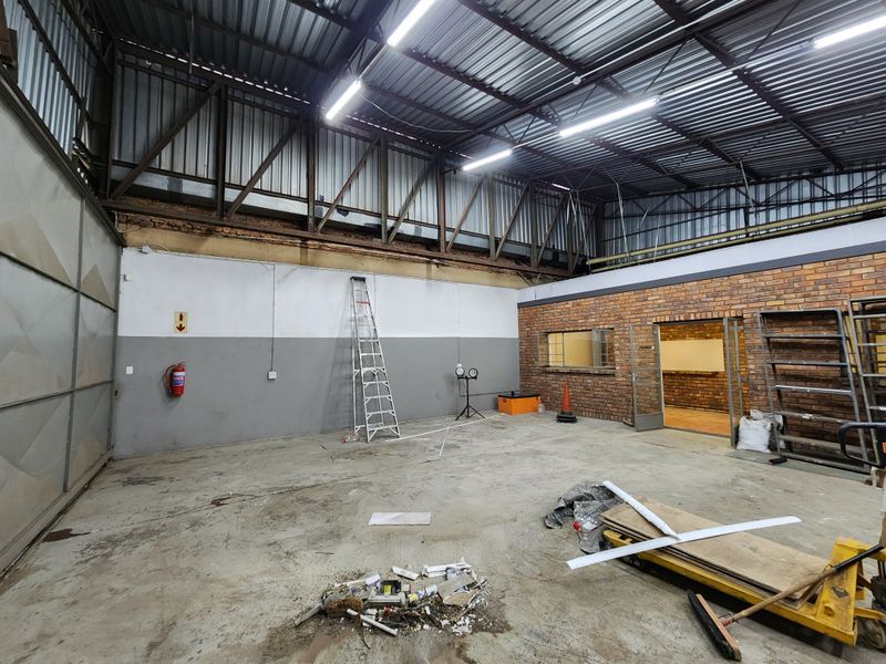 Spacious industrial utility area featuring exposed steel roof trusses, concrete flooring, and brick wall accents, suitable for workshop or storage use.