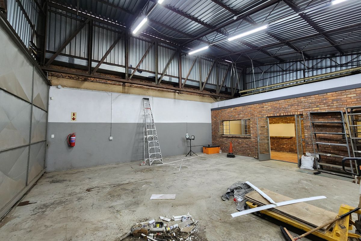 Spacious industrial utility area featuring exposed steel roof trusses, concrete flooring, and brick wall accents, suitable for workshop or storage use.