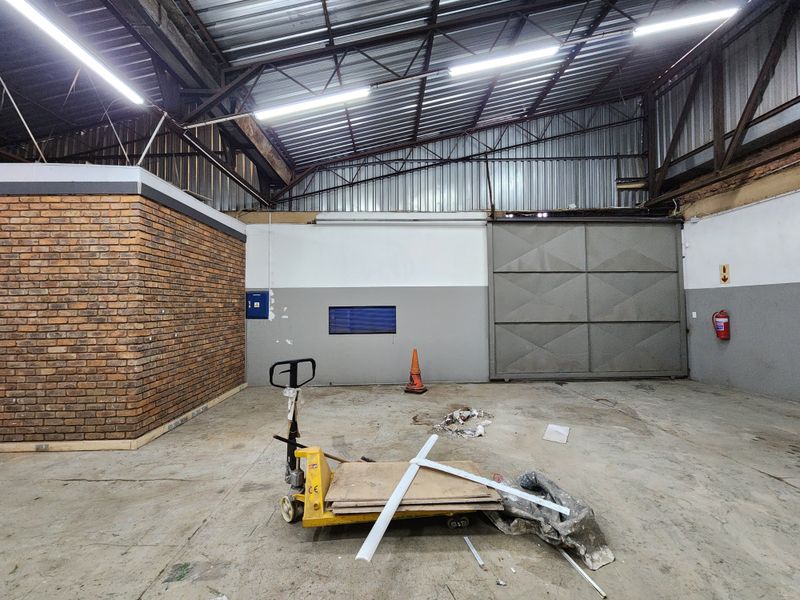 Spacious industrial utility area featuring high ceilings with exposed steel trusses, concrete flooring, and a large sliding access door.
