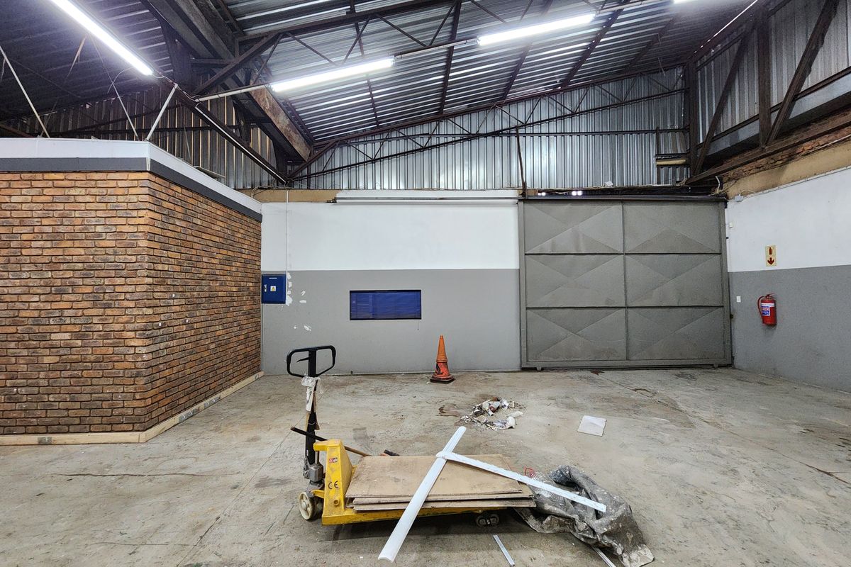Spacious industrial utility area featuring high ceilings with exposed steel trusses, concrete flooring, and a large sliding access door.