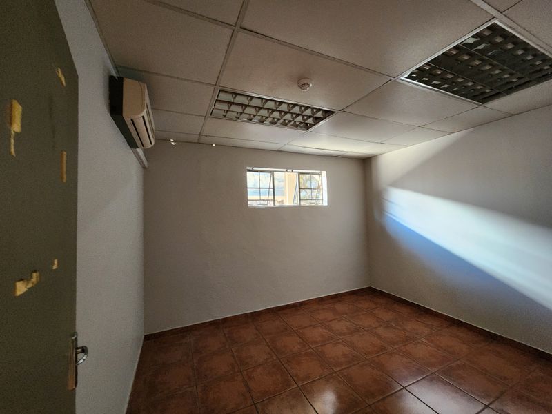 An empty office space featuring ceramic tile flooring, a suspended ceiling with recessed lighting, and a wall-mounted air conditioning unit.
