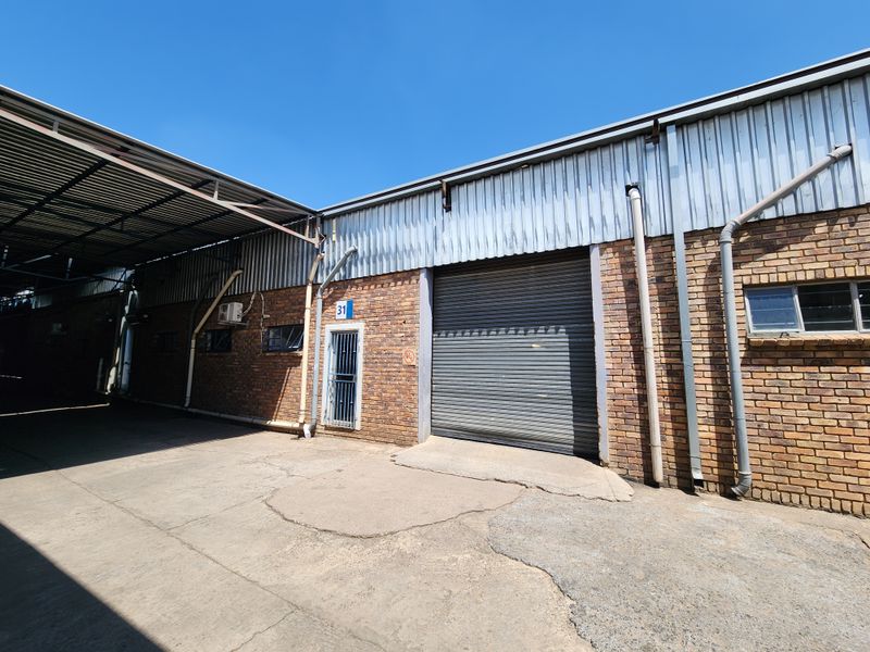 Industrial exterior view featuring a large roller shutter door, brick facade, and concrete apron, providing functional access for loading and operations.