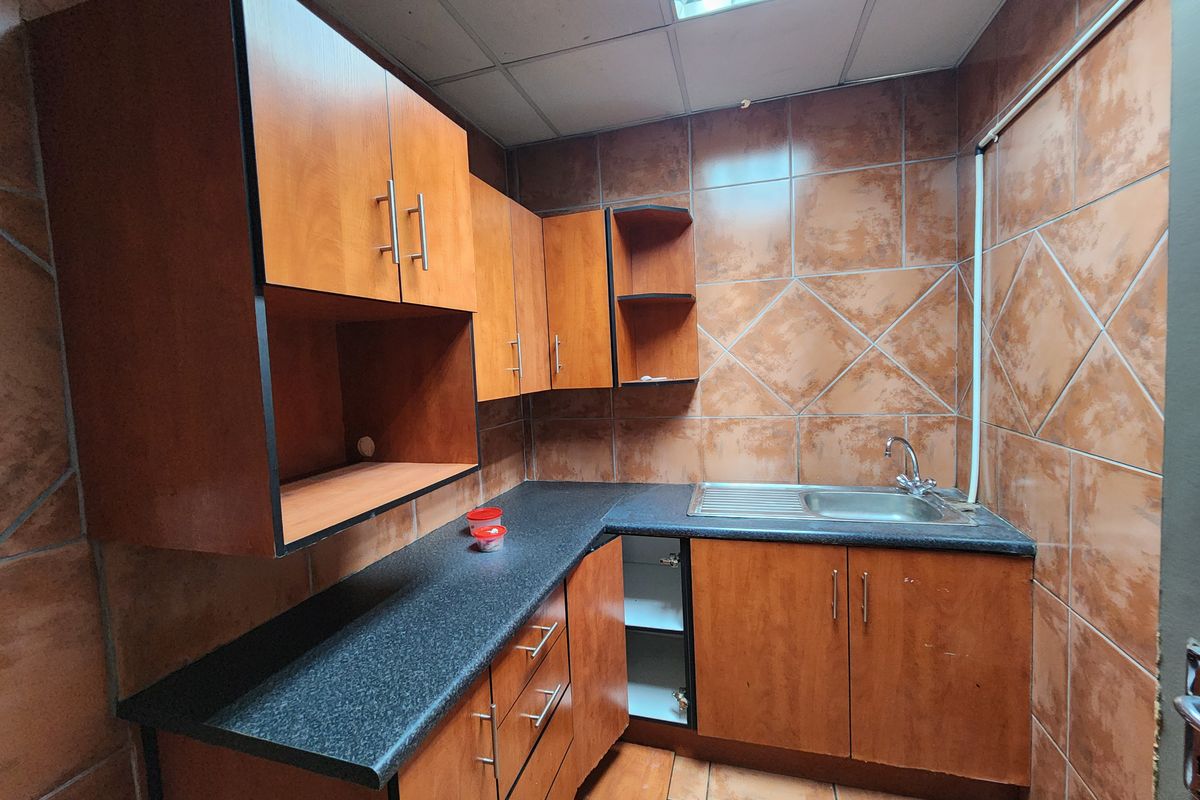 A compact industrial kitchen area featuring wood-look cabinetry, dark laminate countertops, a stainless steel sink, and full-height wall tiling.
