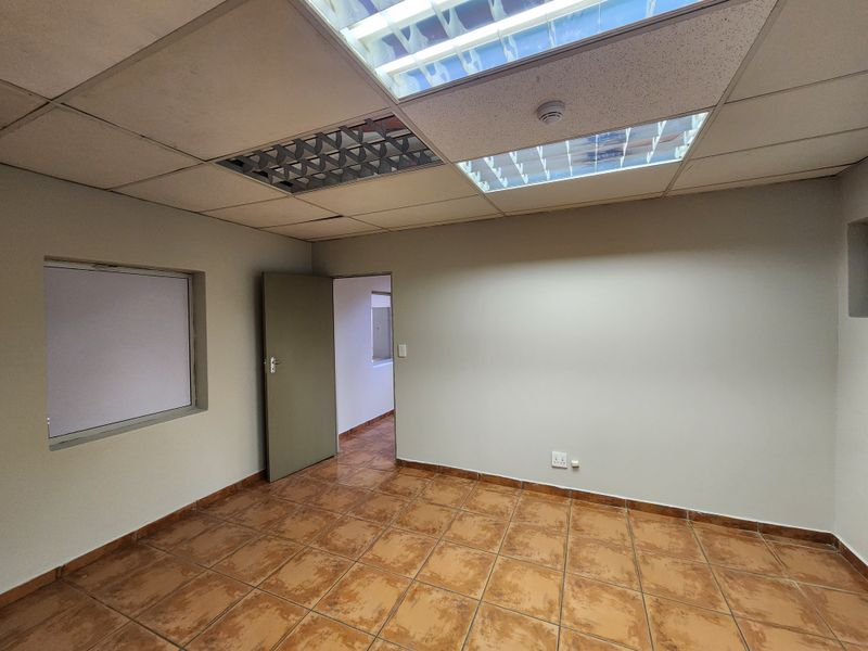 An empty office space featuring ceramic tiled flooring, a suspended ceiling with integrated lighting, and neutral wall finishes.