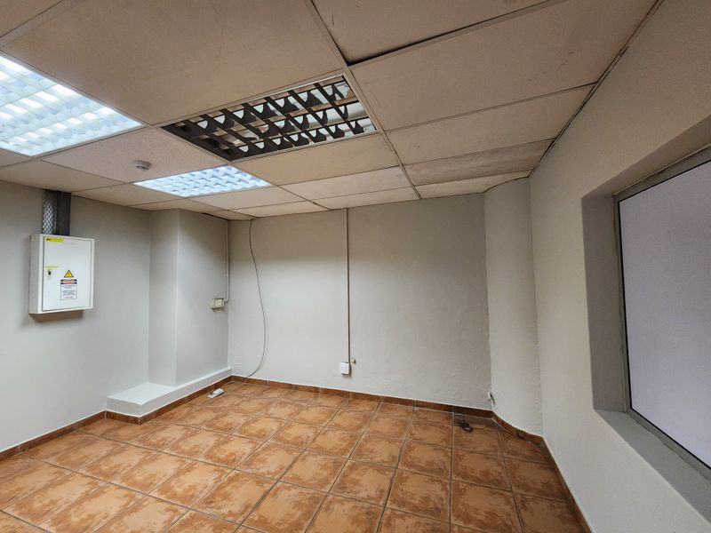 An empty industrial office space featuring ceramic tiled flooring, a suspended ceiling with integrated lighting, and a wall-mounted electrical distribution board.