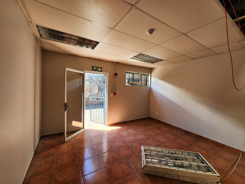 An empty industrial utility space featuring ceramic floor tiles, a suspended ceiling with recessed lighting, and direct access to an exterior security gate.