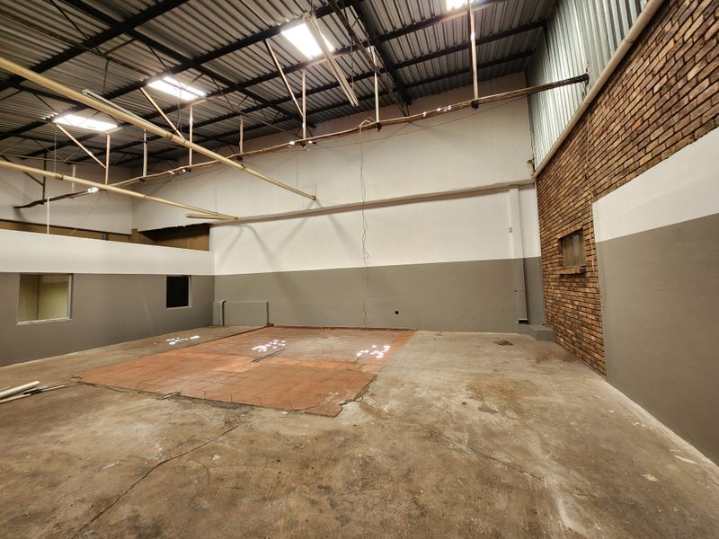Spacious industrial utility area featuring exposed steel roof trusses, a combination of concrete and tiled flooring, and a prominent exposed brick feature wall.