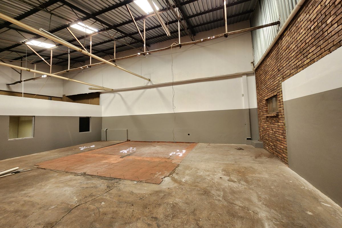 Spacious industrial utility area featuring exposed steel roof trusses, a combination of concrete and tiled flooring, and a prominent exposed brick feature wall.