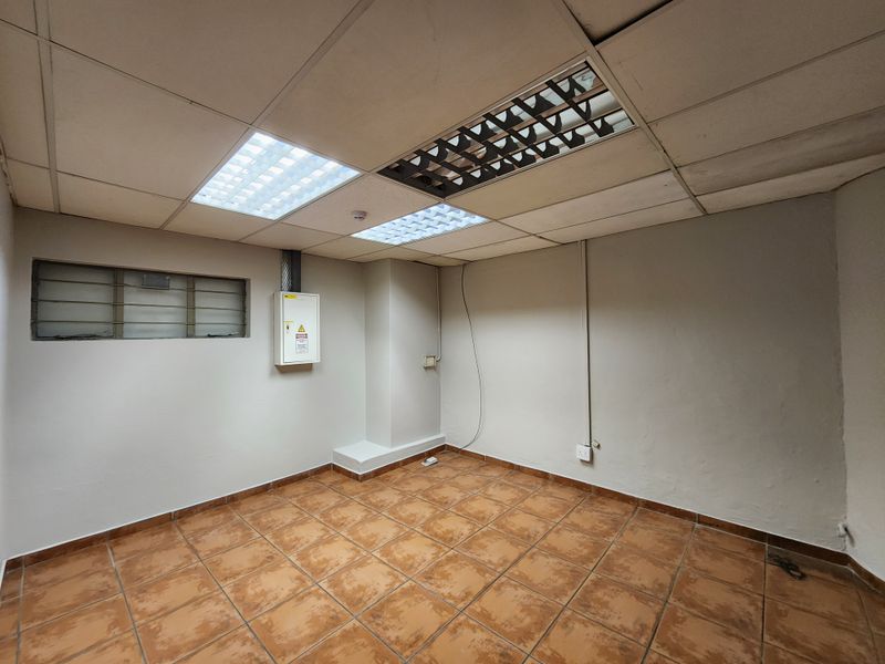 An empty utility or office space featuring tiled flooring, a suspended ceiling with integrated lighting, and a wall-mounted electrical distribution board.