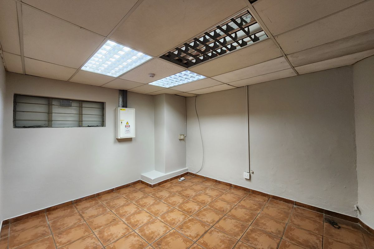 An empty utility or office space featuring tiled flooring, a suspended ceiling with integrated lighting, and a wall-mounted electrical distribution board.