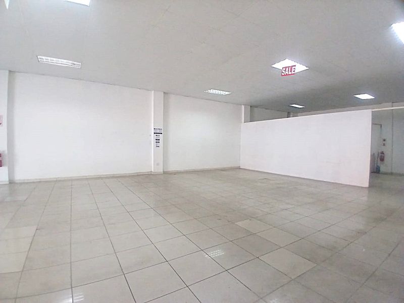 A spacious, empty open-plan retail unit featuring tiled flooring, recessed ceiling lighting, and a neutral white interior finish.