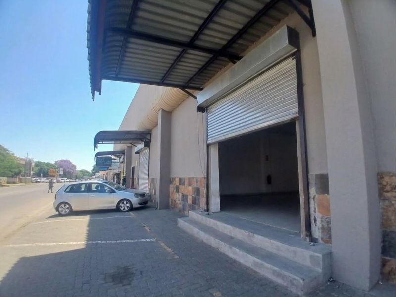 Front exterior view of a retail unit featuring a roller shutter door, metal awning, and stone cladding accents with adjacent paved parking.