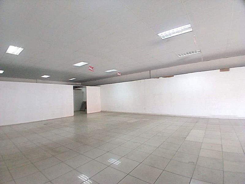 A spacious, vacant retail unit featuring tiled flooring, a suspended ceiling with recessed lighting, and open-plan layout suitable for various commercial applications.