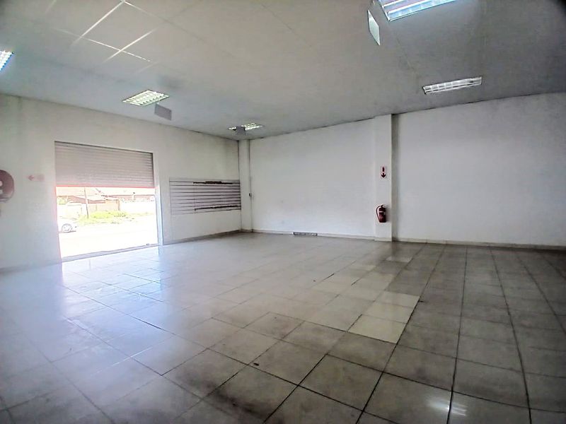 An open-plan retail space featuring tiled flooring, a suspended ceiling with recessed lighting, and a secure roller shutter entrance.